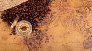 Coffee beans spilling on a world map. A compass rests atop the map.